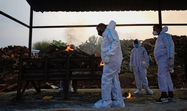 Men wearing PPE (Personal Protection Equipment) perform the last rites of a deceased relative in a ...