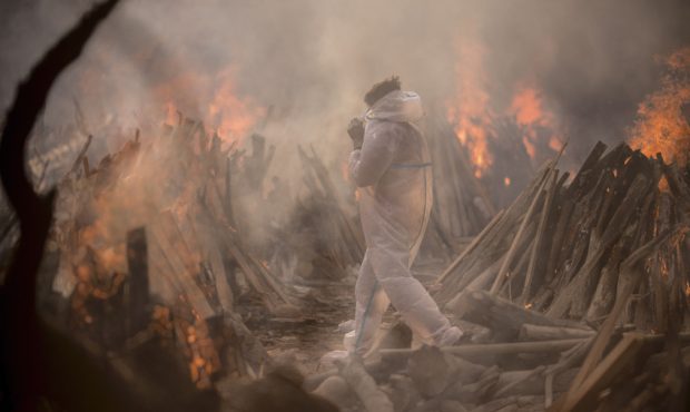 A worker wearing a PPE (Personal Protective Equipment) suit is seen amid the burning funeral pyres ...