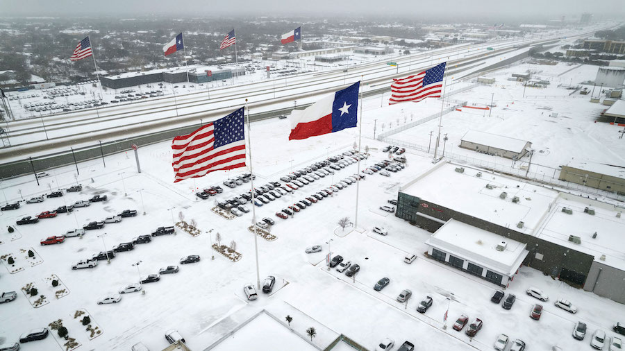 Flags fly over car dealerships as light traffic moves through snow and ice on Route 183 in Irving, ...