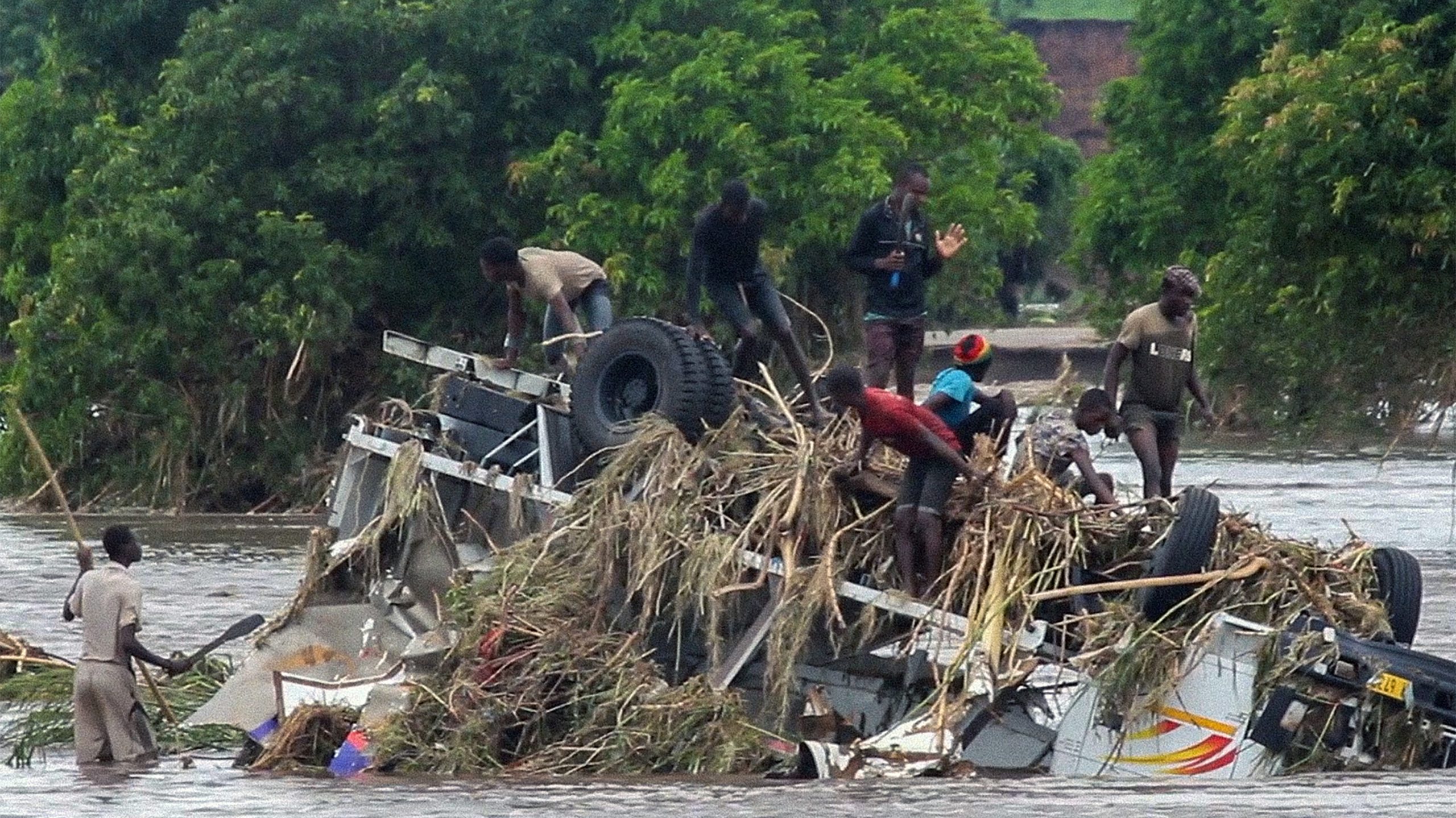 FILE - In this image made from video, people stand on an overturned vehicle swept by flooding water...