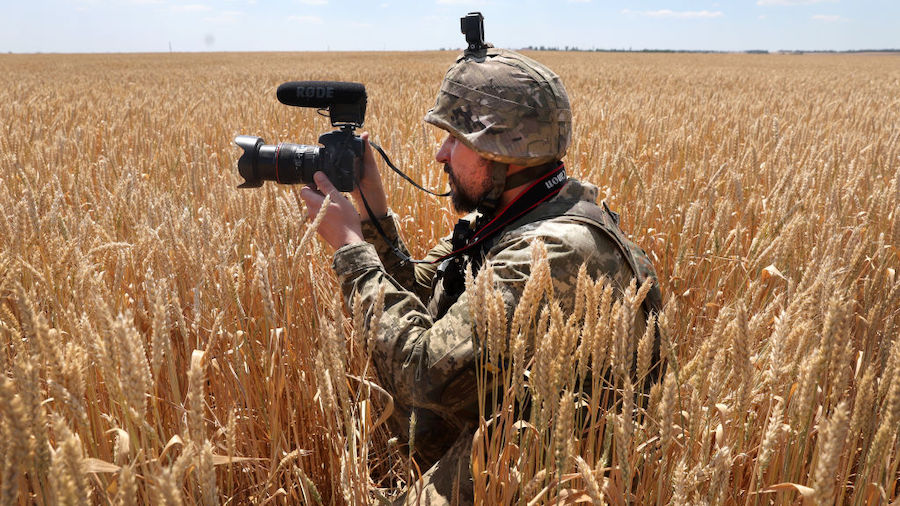 A Ukrainian military journalist takes cover in a wheat field as he captures video while a tank team...