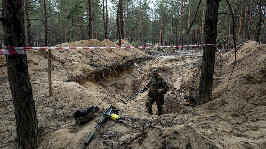 A Ukrainian serviceman uses a metal detector to inspect a mass grave in the recently retaken area o...