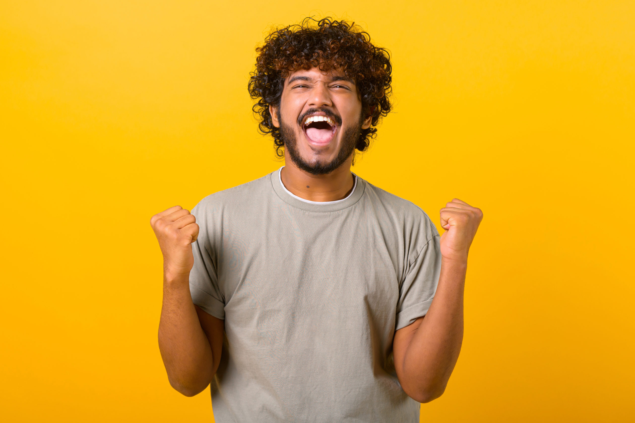 Overjoyed crazy happy Indian curly guy screaming yes in ecstatic, raising fists up