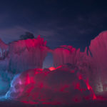Ice formations are illuminated in reds and blues, highlighting unique shapes like stormy clouds and archways between them. (AJ Mellor, Ice Castles)