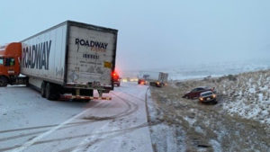 Two semi trucks and multiple cars are off the roads and blocking the roadway.