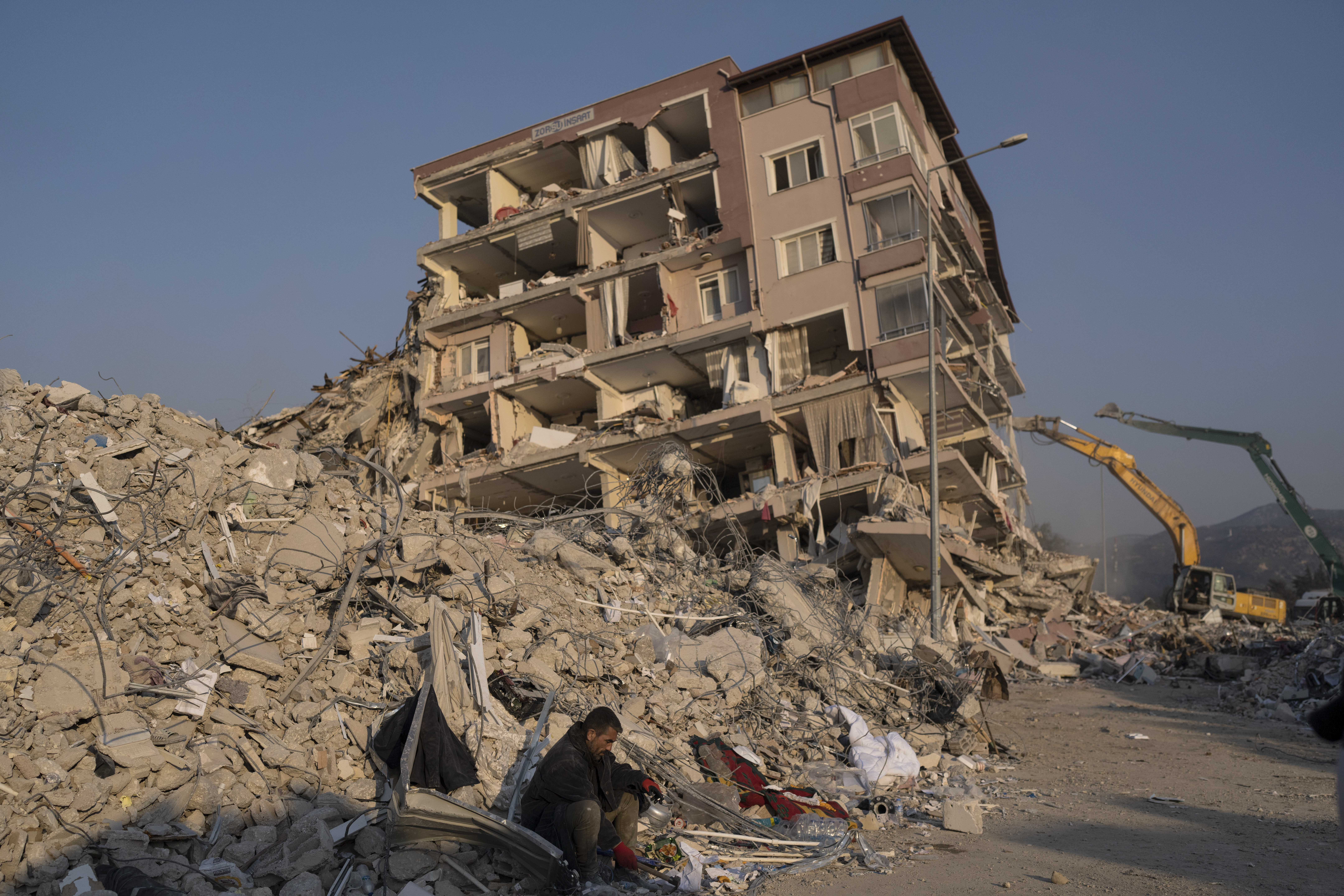 A man sits in the rubble of collapsed collapsed building in Antakya, Turkey, Sunday, Feb. 12, 2023....