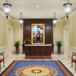 The colonial design accentuates the foyer of the Richmond Virginia Temple. A nod to Jeffersonian motifs is found in the richly-colored area rug that displays a period-correct octagon pattern incorporated with the dogwood blossom (the Virginia state flower). One hundred-year-old repurposed art glass from a protestant church depicting Jesus with His sheep greets visitors upon entering. (Intellectual Reserve, Inc.)