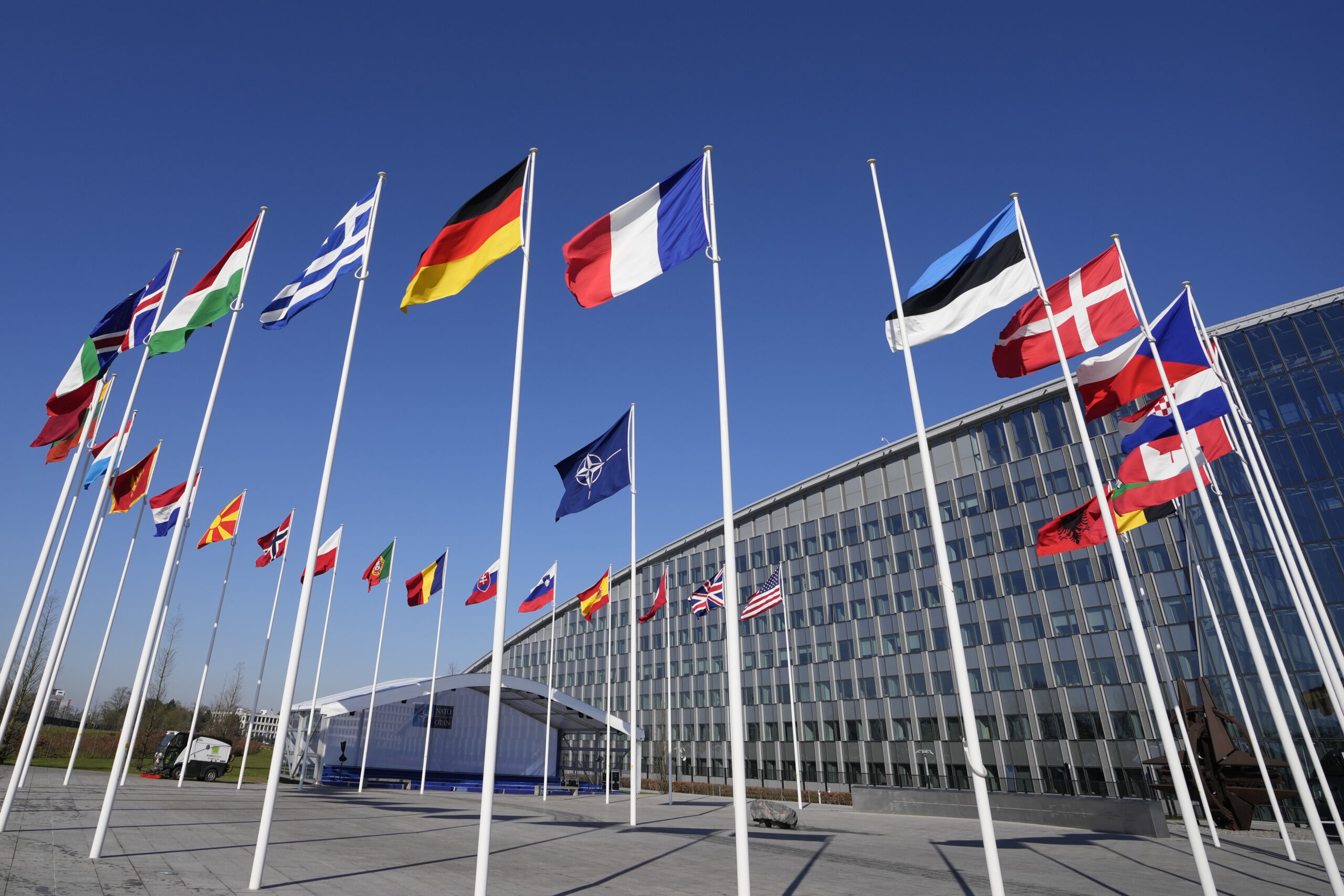 An empty flagpole stands between the national flags of France and Estonia outside NATO headquarters...